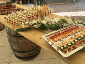 Buffet apéritif de mariage en extérieur avec verrines et canapés, disposé sur une table en bois décorée de fleurs, préparé par Royam pour un événement festif