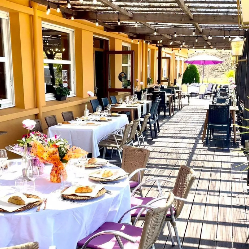 Terrasse du restaurant dressée pour un événement, sous pergola, tables élégamment décorées